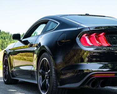 Schwarzer Ford Mustang auf Landstraße, tief fotografiert, zeigt Rückleuchten, Felgen 