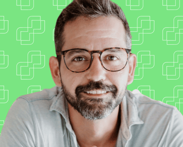 A professional headshot of Michael Franco with a green background. He is in a blue shirt and wearing glasses.