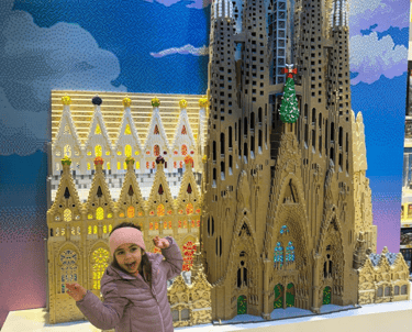 a little girl standing in front of a lego - like building