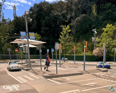 a young boy walking across a street with a car parked in front of him in the Tibidabo traffic park