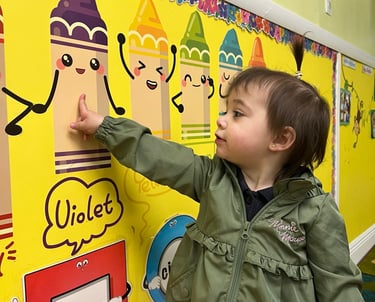 a young child is pointing at a wall with a crayon FANTASTICLANDLEARNING CENTER