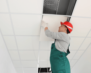 a man in a red hat and overall installing a suspended ceiling