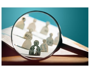 Magnifying glass showing paper cut outs of people on a work desk