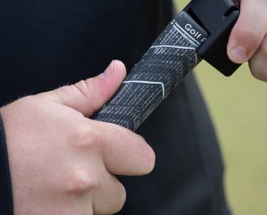 A golfer's hands adjusting a black golf grip tool, Teezup, on the handle of a club, focusing on the grip and tool in use.