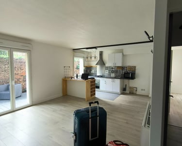 Modern open concept apartment with hardwood floors, a white kitchen, and travel luggage.