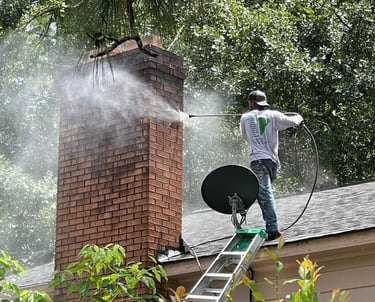 Man wearing a Garnet Painting Company T-shirt pressure washing the chimney of a house.