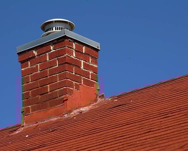 red brick chimney with a metal cap on a red tiled roof against a clear blue sky