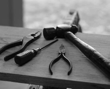 various tools, including pliers, a screwdriver, and a hammer, resting on a wooden surface