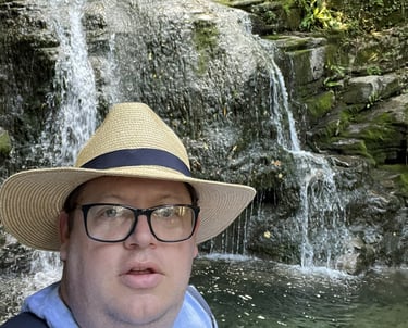 John Grimwood, operations director, in a Panama hat and dark glasses, in front of a waterfall.