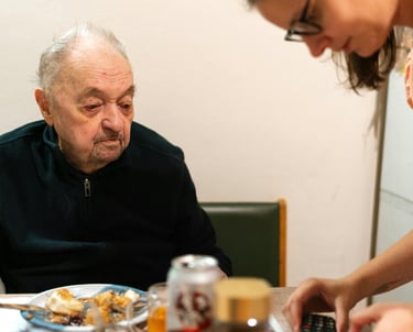 une personne âgée assise autour d'une table regardant son aidante manipuler son portable.