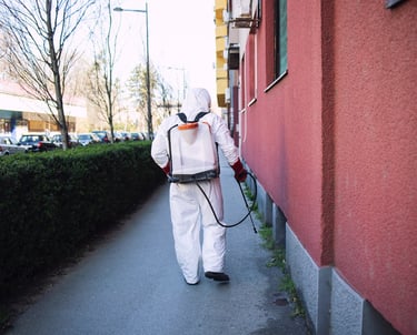 Un technicien en combinaison de protection blanche pulvérise un traitement fongicide sur une façade