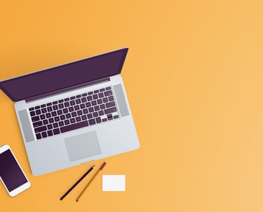 An overhead shot of a vibrant sherbert orange surface with an open laptop, cell phone, pens/pencil