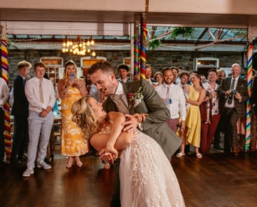 First dance dip at Plas Dinam Country House, the couple beaming as guests cheer them on in the vibrant reception hall.