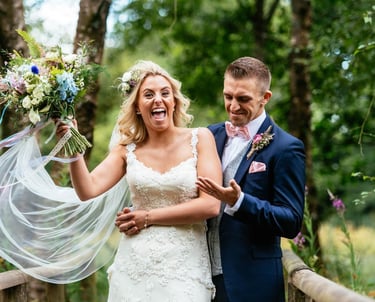 Bride and groom laughing on wooden bridge at Llanerch Vineyard wedding in South Wales, captured candidly by Owen Mathias