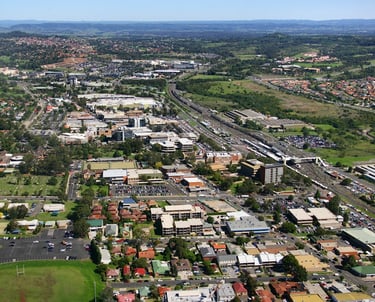 Aerial view of Campbelltown NSW showing urban buildings, railway lines, parks, and surrounding