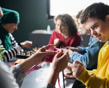 A group of people engaged in a social activity around a table, demonstrating NDIS community access