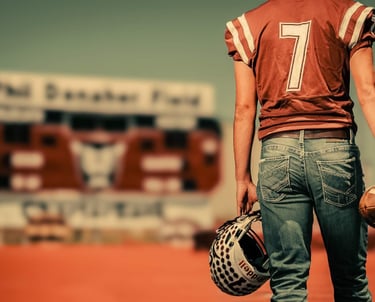 a high school graduate in a football uniform holding a football helmet