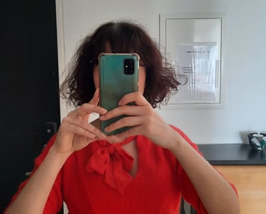 Selfie allo specchio con top rosso e smartphone verde che copre il volto