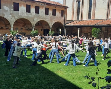 Persone in cerchio su prato, si tengono per mano e danzano in Museo