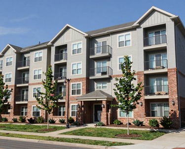 A vibrant mural covers the upper section of a multi-story building. The artwork features geometric patterns and a variety of bright colors including teal, pink, yellow, and orange. Below, a green sign indicates a job center. People are visible at ground level, walking past the building. A person is elevated on a cherry picker, possibly engaged in work on the mural.