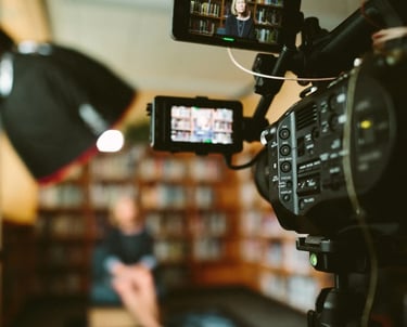 A camera pointing to an author sitting in front of a library