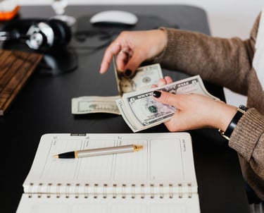 woman holding money in her hand with a pen and paper on desk as she budgets and manages money