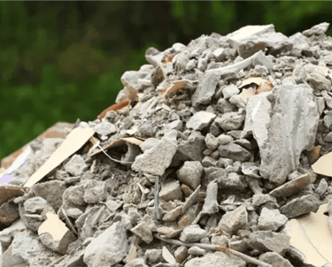 Pilha de entulho cinza com restos de concreto, tijolo e cerâmica, pronto para ser removido com caçam