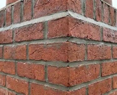 Close-up of a red brick chimney with fresh mortar repointing on a residential rooftop.