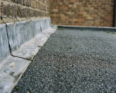 Close-up of lead flashing installation on a flat felt roof against a brick wall.