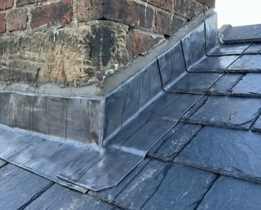 Professional lead flashing installation around a brick chimney on a grey slate roof.