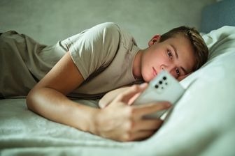 a young boy is laying on a bed with a mobile phone