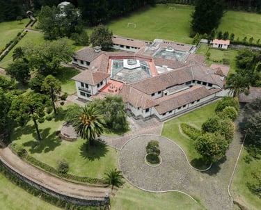 Fotografía con dron de mansión colonial de paredes blancas con techo naranja, cúpulas rodeada de naturaleza Quito Ecuador
