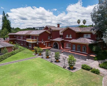 Fotografía aérea de gran casa religiosa de color rojo rodeada de hermoso jardín verde en Quito Ecuador