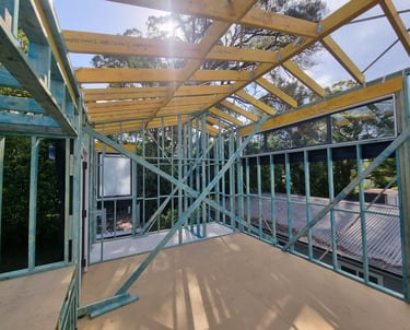 Construction site showing timber roof trusses and wall framing for a new house addition.