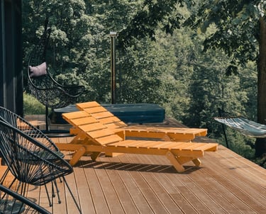 Modern wooden deck with yellow lounge chairs, a hot tub, and a hanging chair overlooking a lush forest.