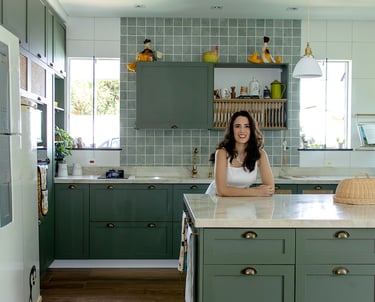 Foto da arquiteta Luciana em uma cozinha clássica com marcenaria verde, bancada de pedra natural e muita iluminação natural