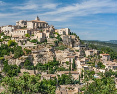 Panoramic view of the hilltop village of Gordes in Provence, France, featuring historic stone buildings and cliffs.