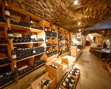 Rustic underground stone wine cellar featuring wooden racks and crates filled with aged wine bottles.