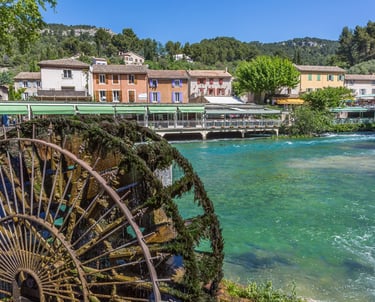 Historic mossy water wheel in Fontaine-de-Vaucluse by the turquoise Sorgue river in Provence, France.