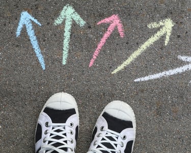 Verschillende gekleurde pijlen op asfaltvloer met gymschoenen die keuzes symboliseren.