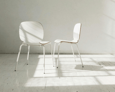 Twee witte stoelen schuin tegenover elkaar met een open ruimte ertussen, symbool voor oudercontact 