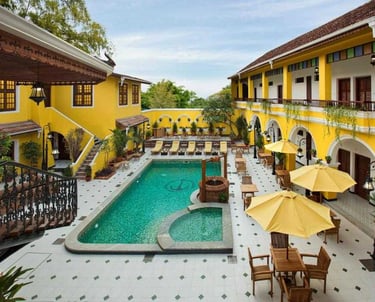 Charming resort in Fort Kochi, Kerala, featuring a vibrant yellow facade, a serene swimming pool, sun loungers, and umbrellas
