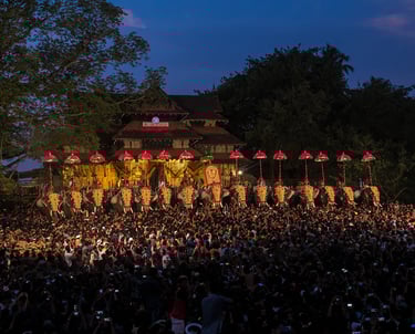 Thrissur Pooram festival celebration with illuminated parasols and a large crowd in front of a traditional temple.