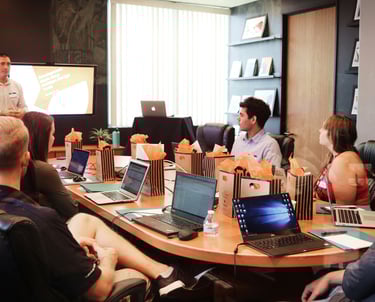 a group of people sitting around a table with laptops