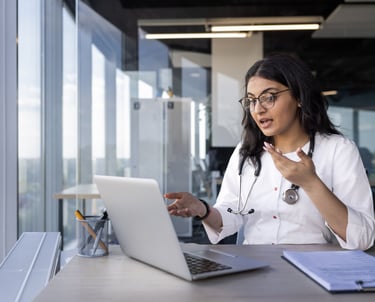 Doctora en consulta de telemedicina interactuando con un paciente a través de una videollamada.