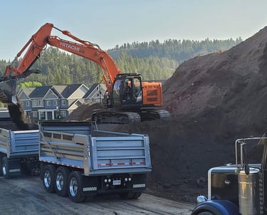 a truck with a large load with an excavator adding to the dirt