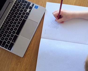 Child writing in an exercise book whilst doing their online tuition to help them with the 11+ test