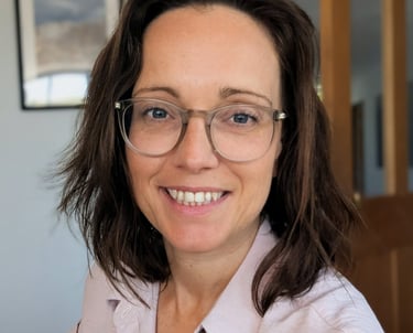 A smiling female kent tutor with brown hair wearing transparent glasses and a pink shirt.