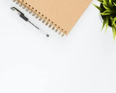 Photo d'un coin de cahier avec un stylo posé à coté et un bout de plante