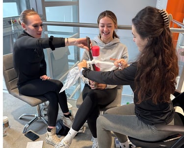 3 people sit together practicing arm bandaging with training materials during a first aid class.